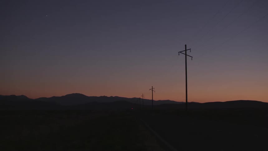 A car drives down a dark road at sunset