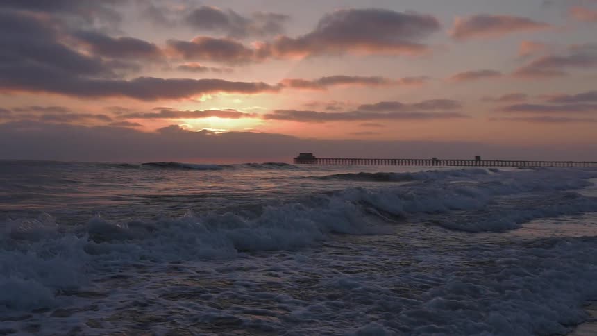 Waves crashing to shore as the sun sets in a cloudy sky