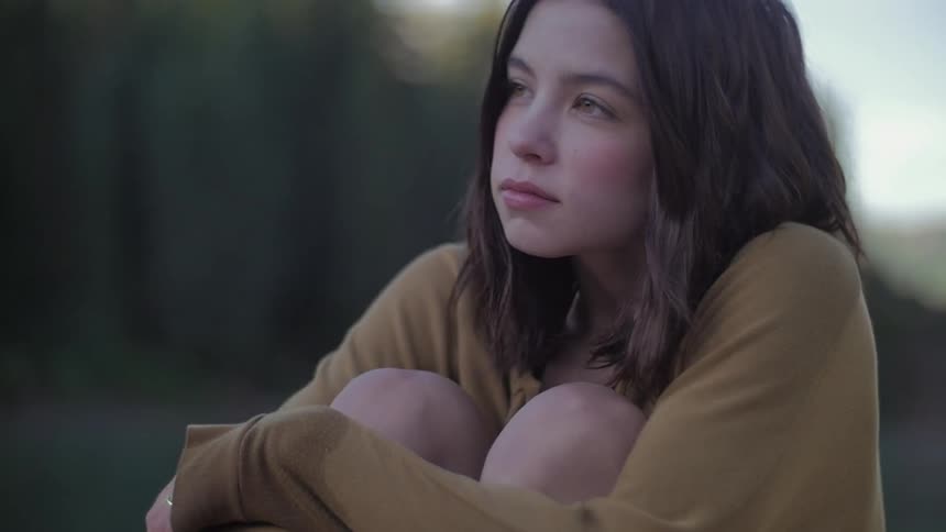 A young girl in a brown shirt holding her knees