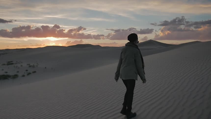 A person climbs up a sand dune at sunset