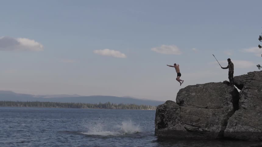 Group of friends jump from a rock into a lake while being filmed