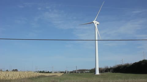 A wind turbine sits beside a road near a field