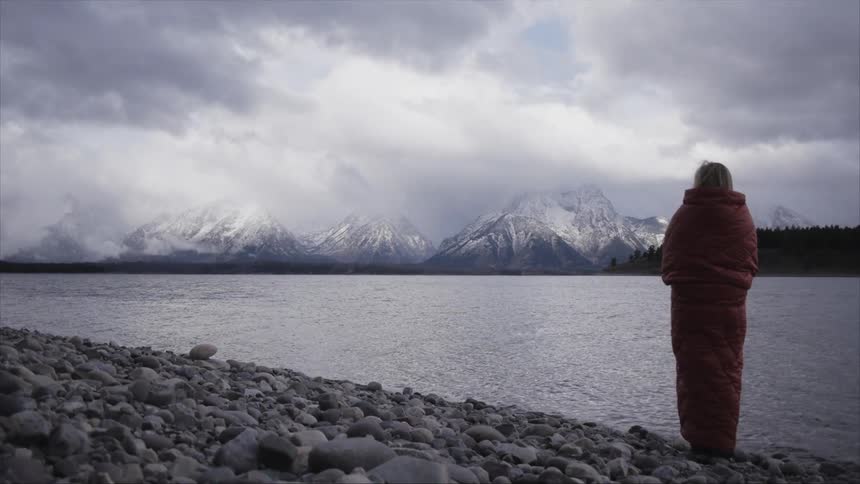 A woman wrapped in a blanket looks towards snow covered mountains