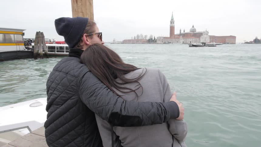A man and a woman hug while sitting on the end of a pier