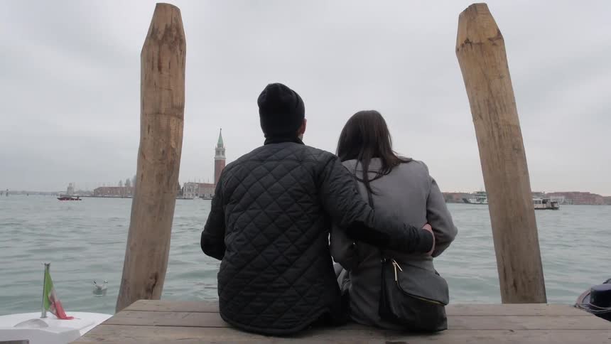 Couple sitting on a pier across the bay from the city