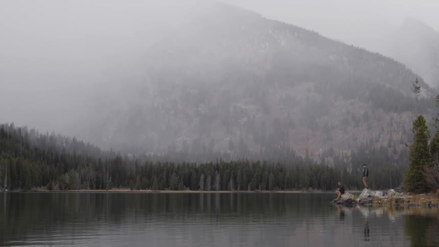 Two people stand on rocks in front of a misty lake