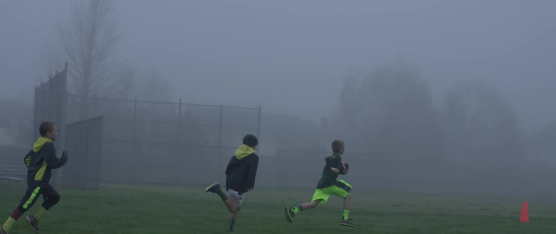 Three boys run through a foggy park