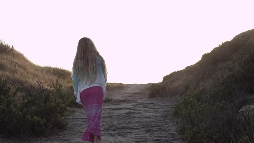 A girl walks a path between hills at dusk