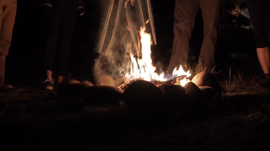 Group stands around a fire lined with rocks