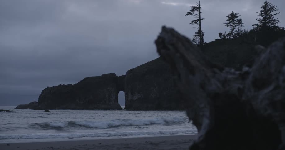 Waves crashing onto a beach surrounded by rocky cliffs on an overcast day