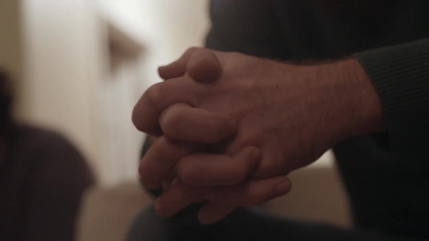 A person sits with their hands clasped