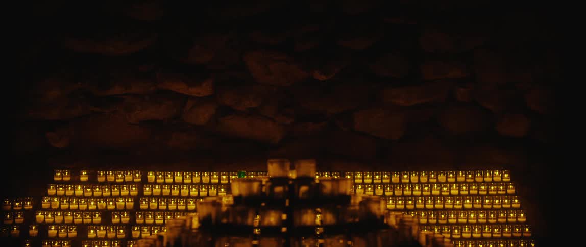 Rows of candles burn in a dark cave