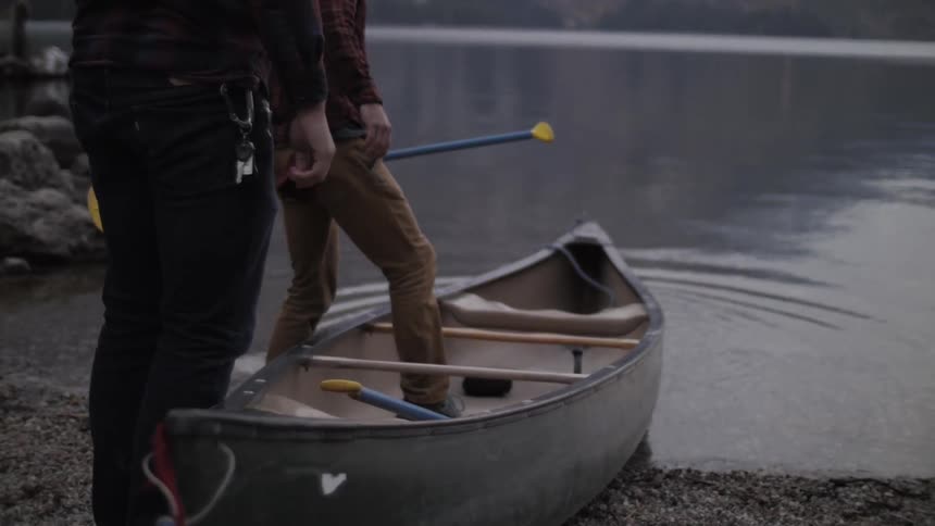 Two men push a canoe into a lake