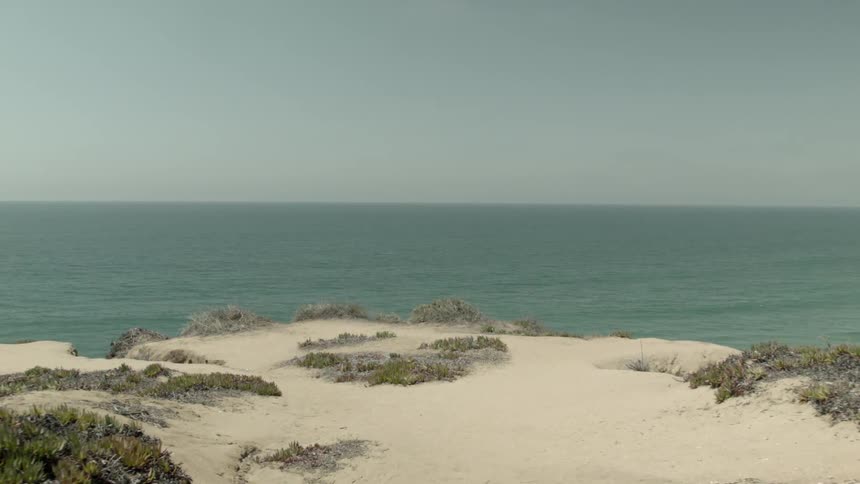 A first person view of walking towards the edge of a sandy cliff next to the water