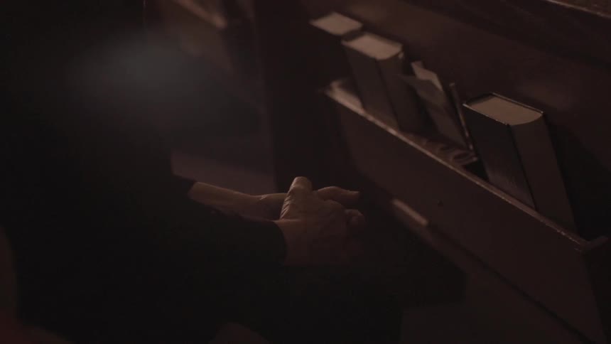 A person sits on a church pew with their hands grasped
