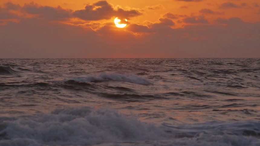 Waves lap onto a beach while the sun sets