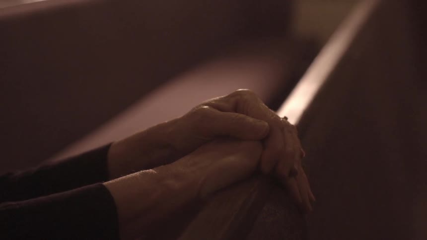 A woman's hands resting on the back of a pew