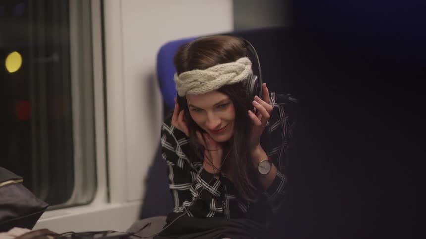 Woman listens to headphones while sitting down at night in a train