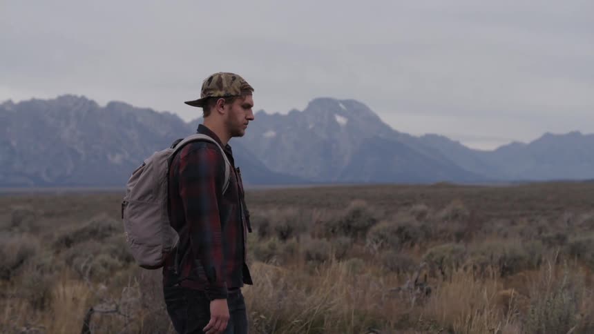 A man in a backpack crosses a shrubby field