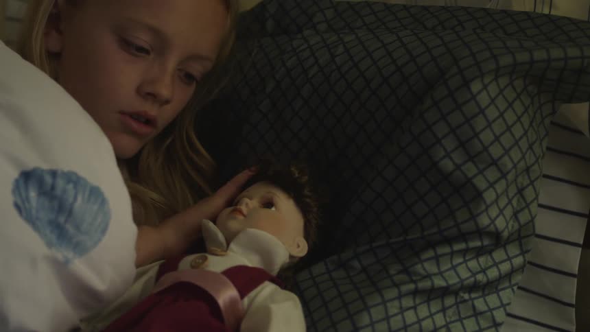 Girl holding a doll lying on a bed