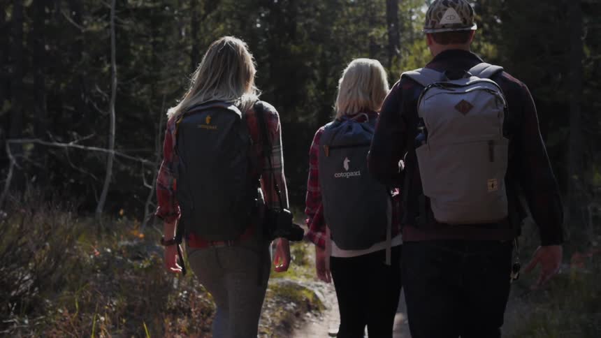 A group of people carrying backpacks walk down a trail