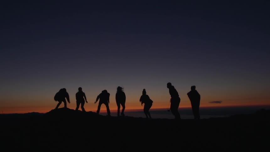 A group of 7 people jumping in a hill at night with the sunset in the background