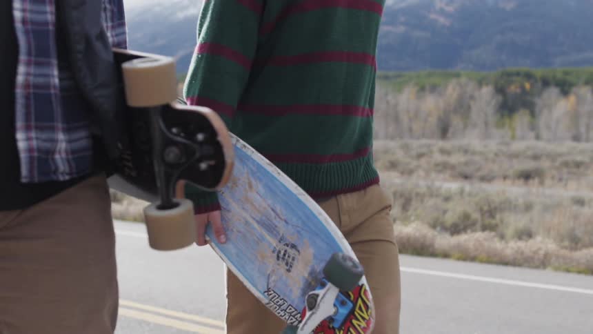 Two teens walking down a paved road carrying their skateboards