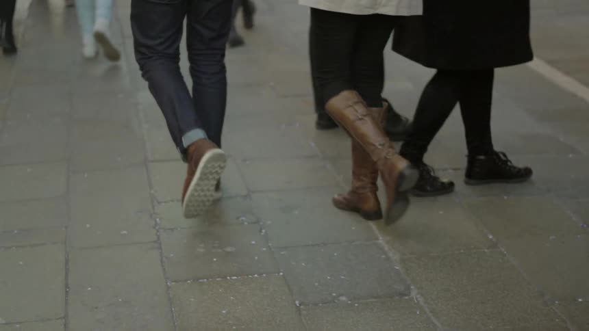 The legs of pedestrians as they walk down a sidewalk