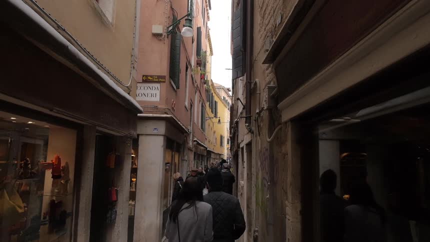 Many people walk down a narrow passage in a city