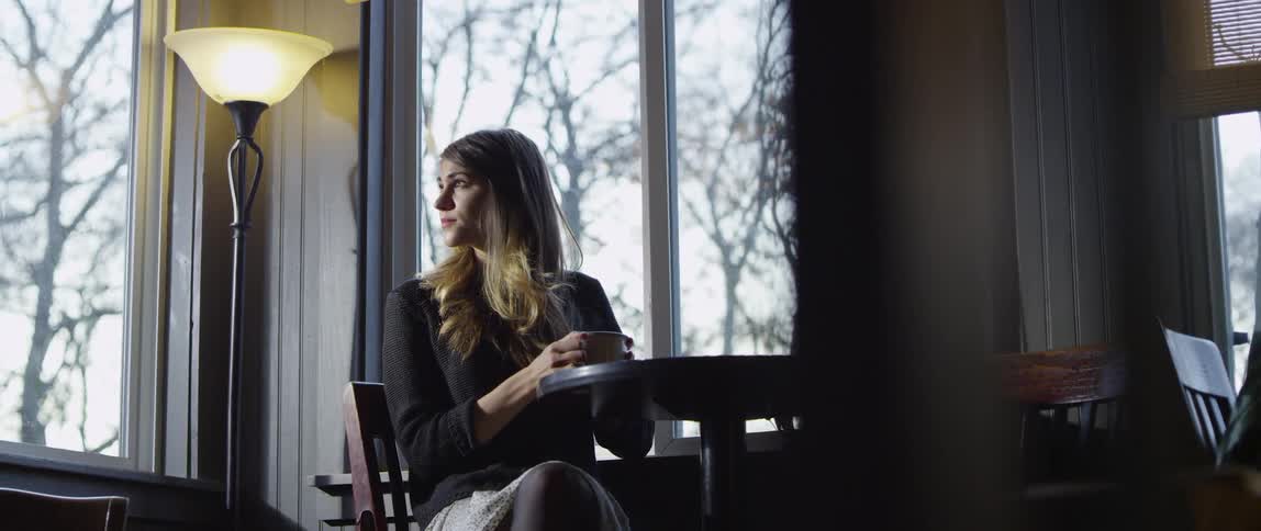 Woman sitting at a table indoors with a mug on a cloudy day