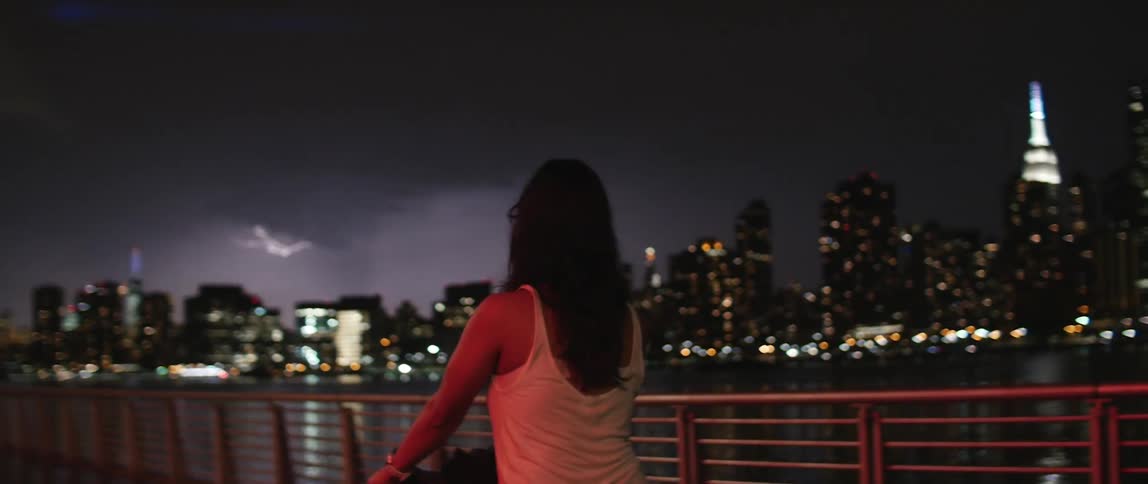A woman watches lightening flash above a city skyline