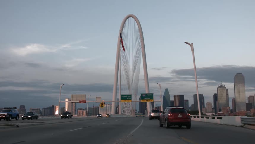 Cars driving down a highway with buildings in the background