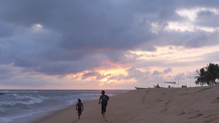 Two boys run on the beach with a sunset in the background
