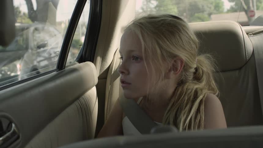 Little blonde girl looks out the window of a moving car