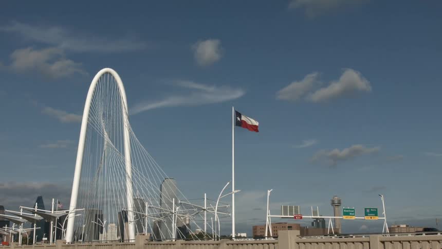Man cars passing by as a flag flies overhead on a clear sky