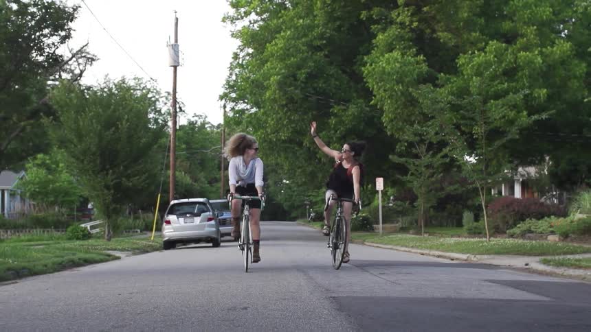 Two women riding bikes down a street on a cloudy day