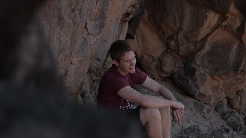 A man sits next to a rock formation
