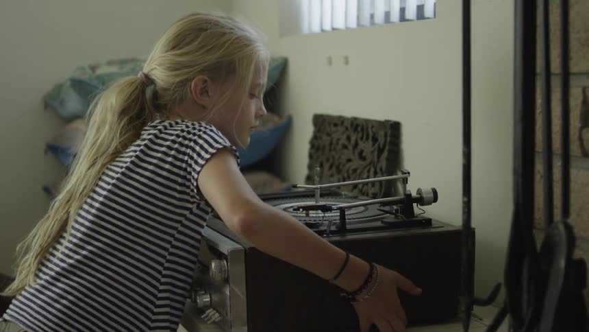 Girl walks over to a record player and moves it