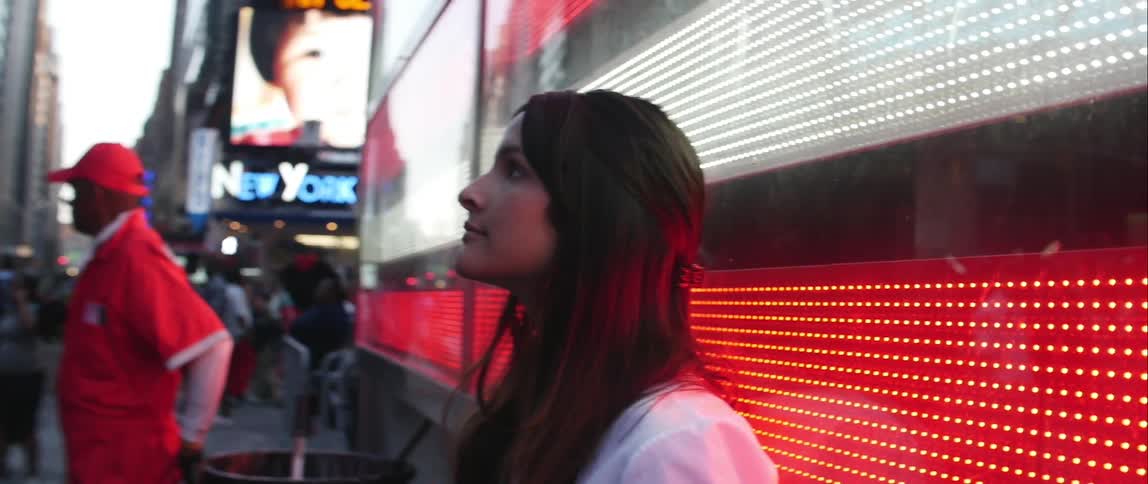 A young woman looking up at lights and signs on a busy new york street