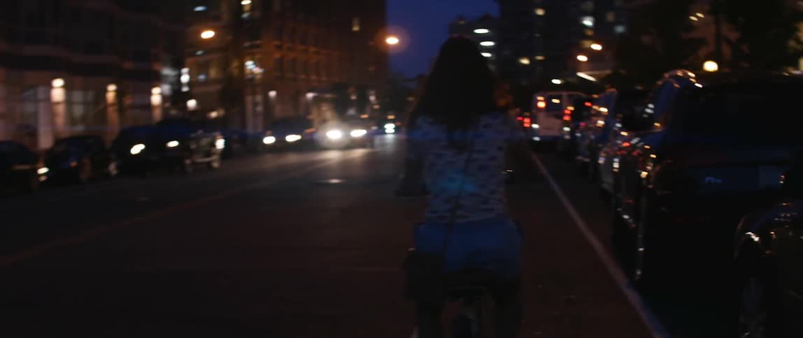 A young woman riding a bicycle down a city street at night