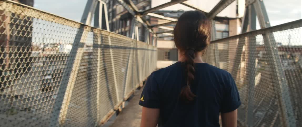 A woman walks down a narrow pedestrian bridge over a city