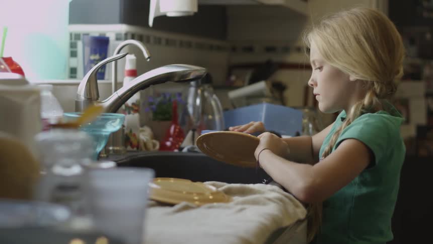 Little girl washes the dishes in the kitchen