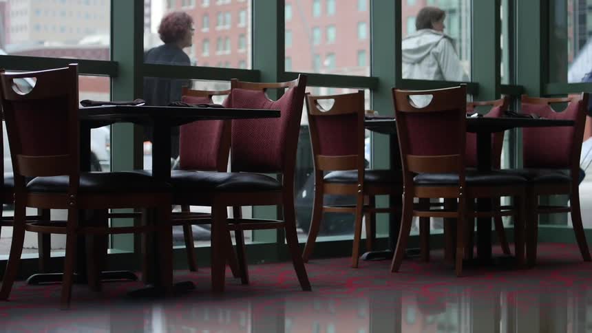 People with suitcases pass outside the windows of an empty urban restaurant