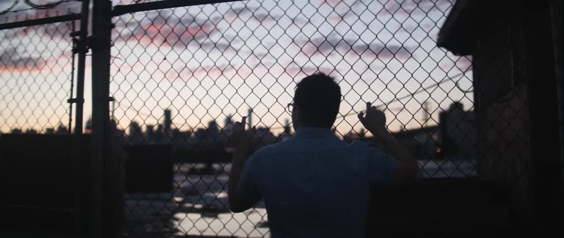 Spectacled man looking at a large city through a fence at desk