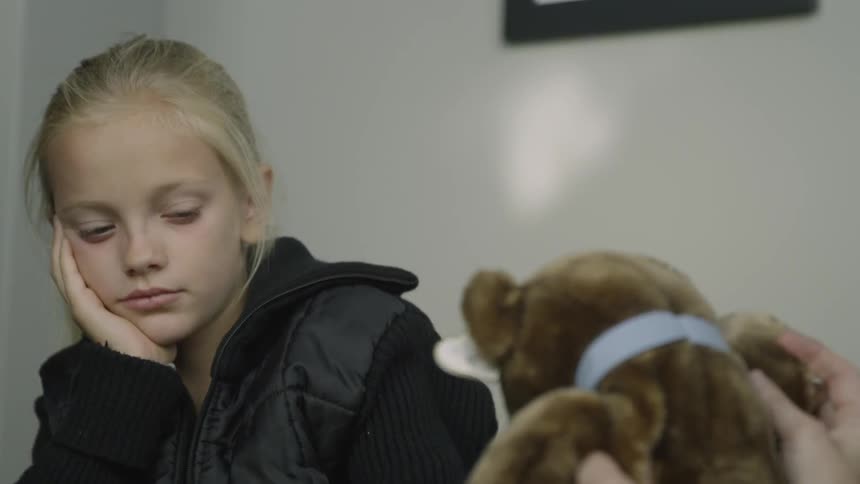 Girl holds her head as she looks at a teddy bear