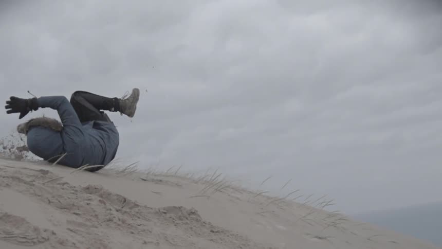 A person falling and rolling down a sand hill