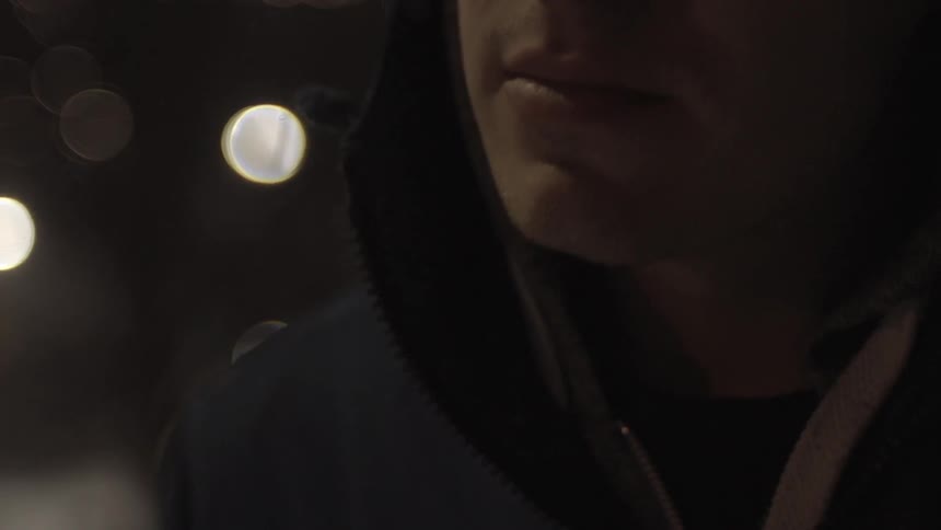 A  man stands outside at night with lights behind him
