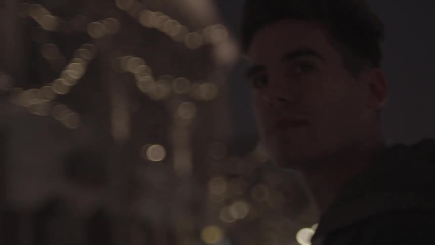 A young man walks through a well-lit downtown street at night