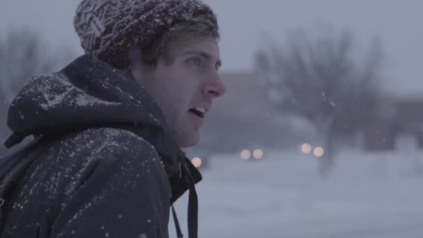 A man stands looking around as it snows