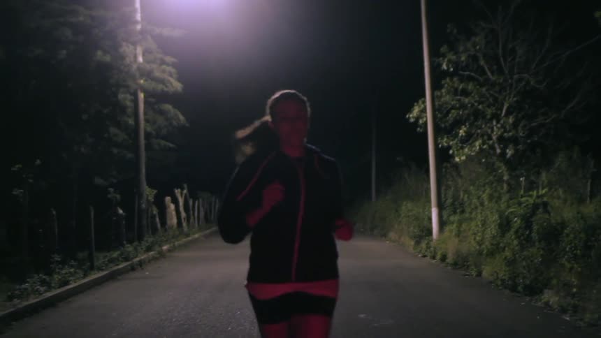 A woman in shorts jogging down a road at night